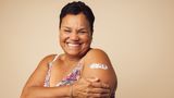 Woman smiles as she shows off the plaster on her arm protecting the spot she received her vaccination