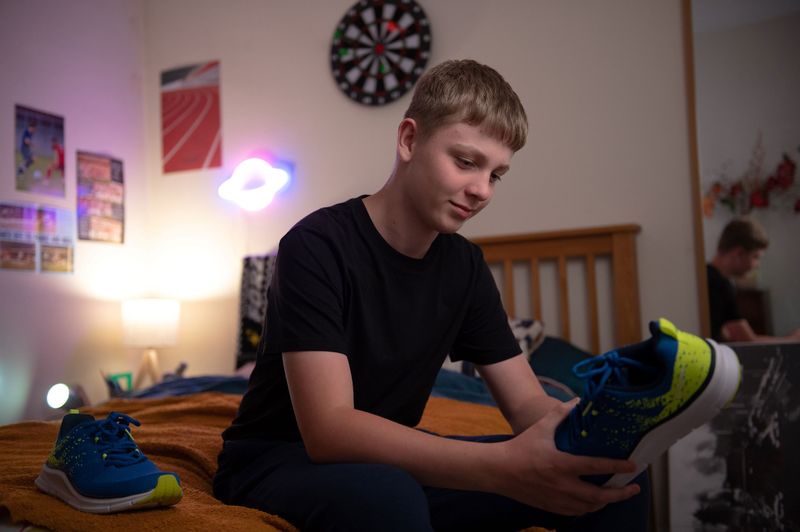 A young boy sitting on the edge of a bed holding a new trainer
