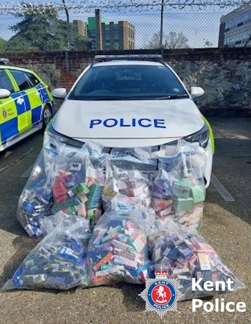 A parked Police car with multiple clear bags of seized illegal tobacco items piled against the front bumper