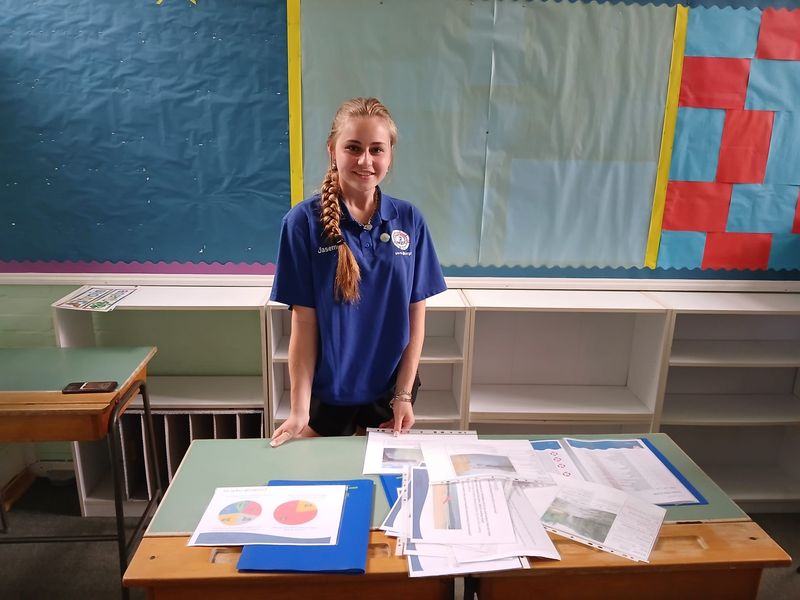 A young person wearing a Gravesham Life Saving Club t-shirt standing behind a desk covered with water safety information
